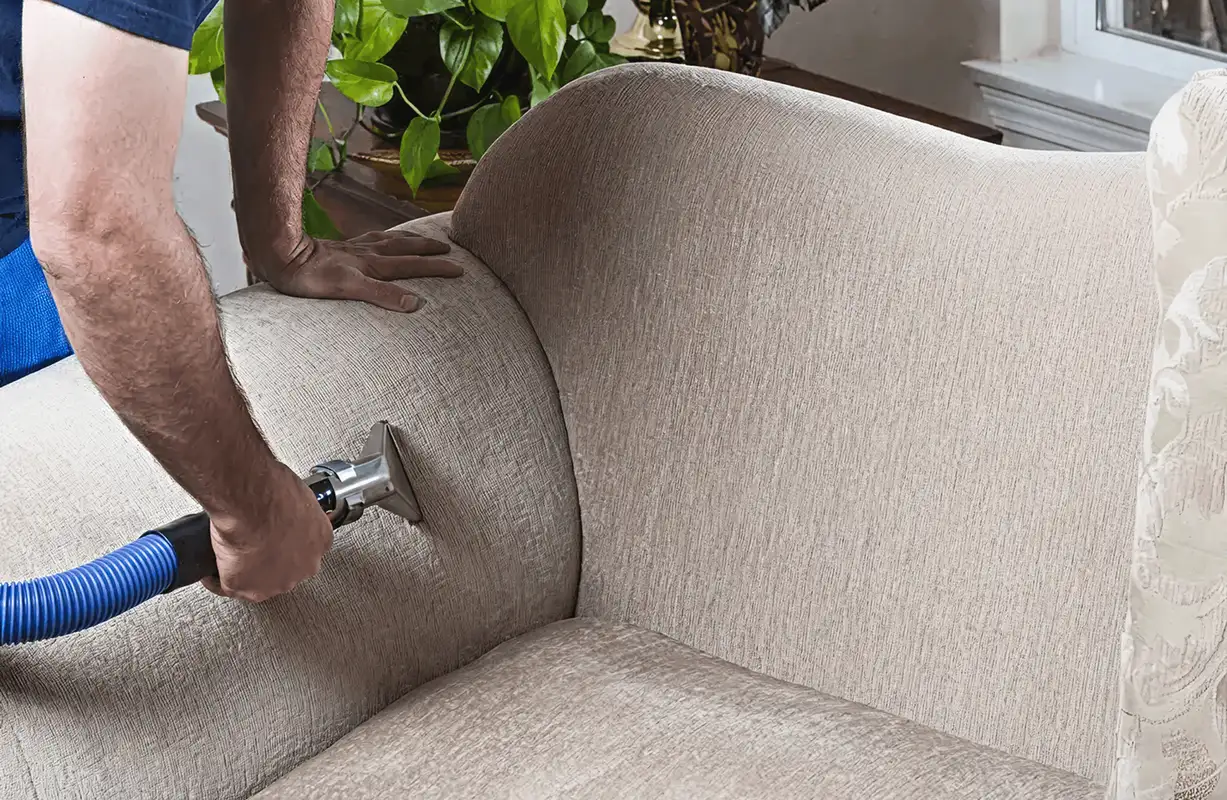 Professional upholstery cleaner deep-cleaning a fabric sofa with a handheld extraction tool and hose, Bradenton, FL.
